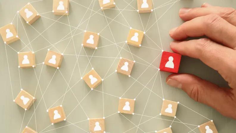 A hand placing a red block with a user icon among interconnected wooden blocks representing a social or business network