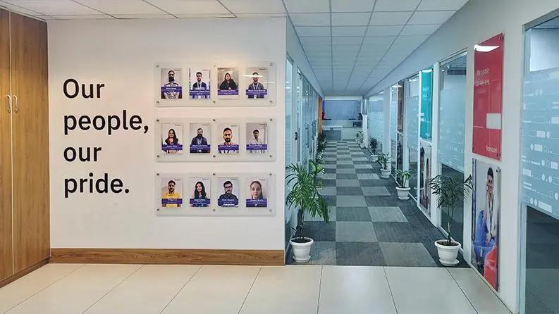 Modern jaipur office hallway with an employee recognition wall displaying team members' photos and the quote 'Our people, our pride