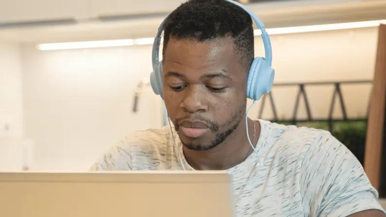 Male customer support agent working on a laptop with headphones.
